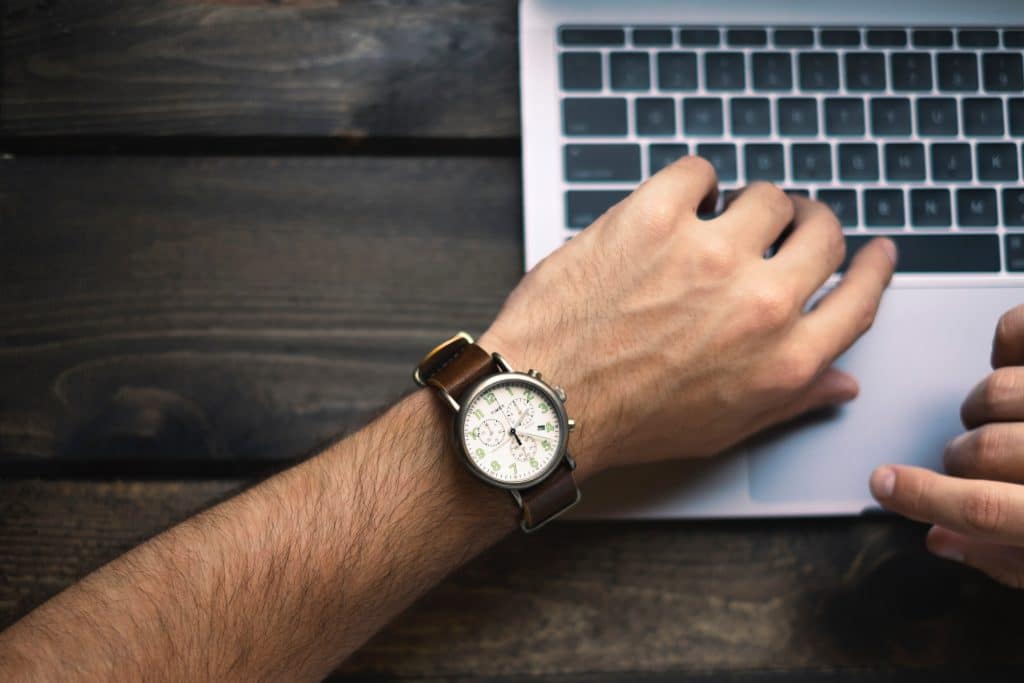 Man checking watch while on computer to understand where he spends his time