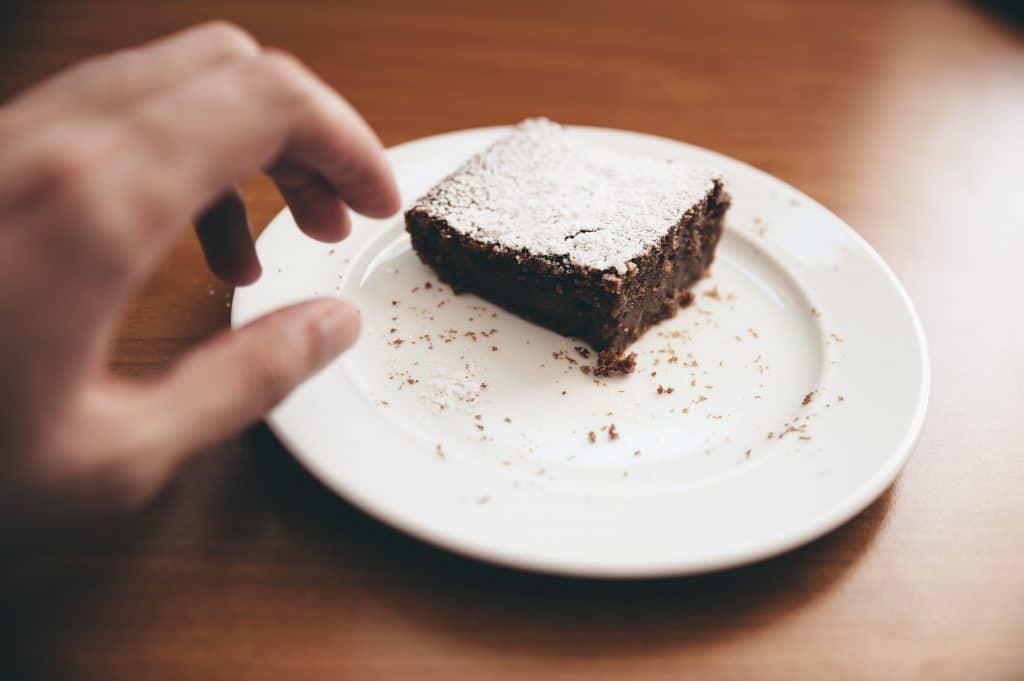 Person reaching for a chocolate brownie on a plate