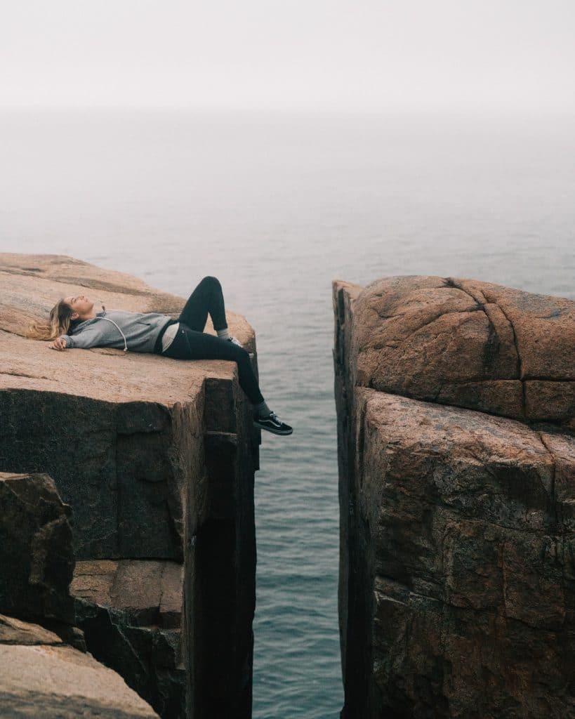 feeling unmotivated - woman laying on edge of cliff unable to bridge the gap