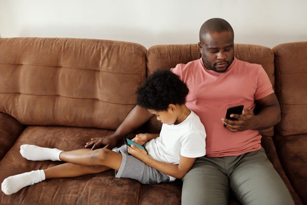 Father and son relax on couch with smartphones