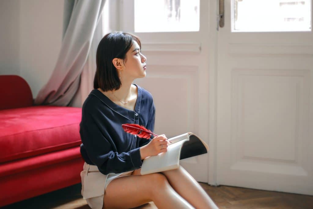 Woman writing in a notepad with red feather and red sofa in background