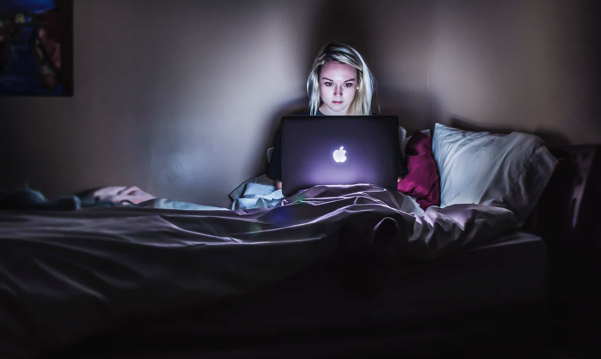 woman doomscrolling laptop computer in bed at night