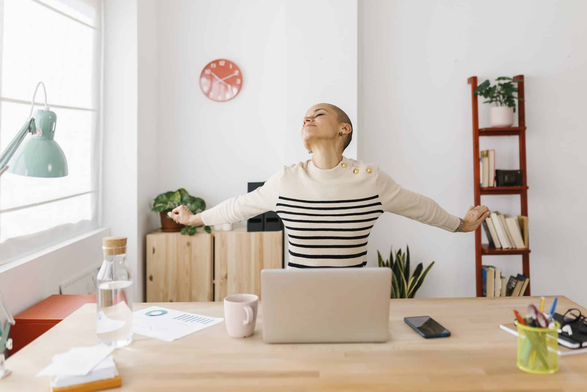 smiling woman stretching at desk while at work wellness