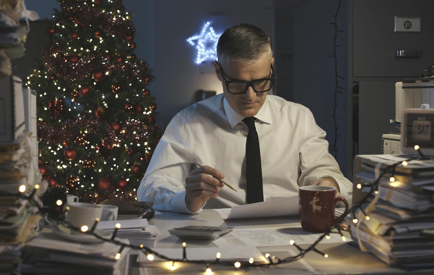 Sad businessman working on Christmas Day, he is surrounded by piles of paperwork