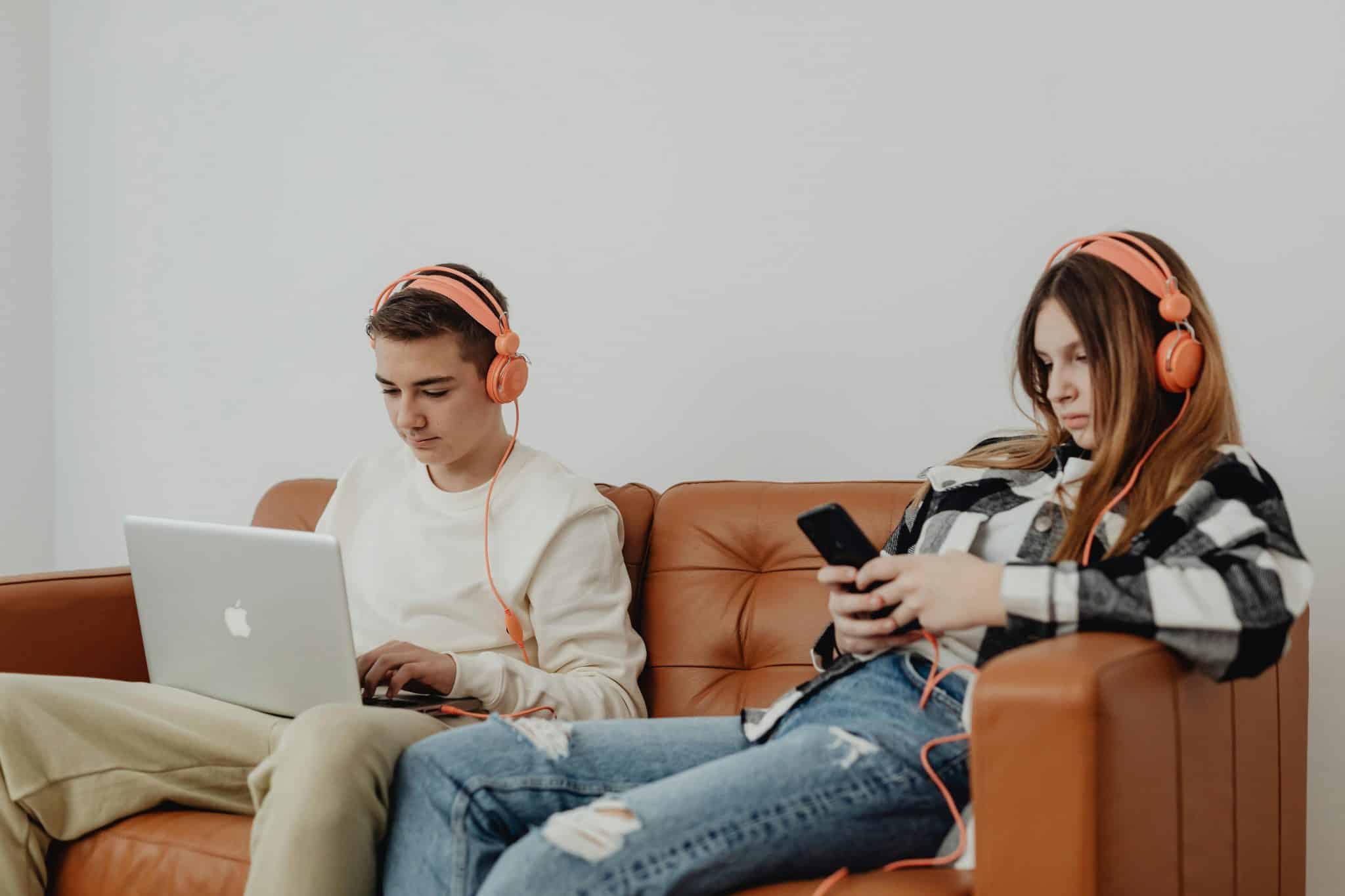 Two people, one scrolling on their phone and the other working on a laptop, both seemingly unaware of each other.