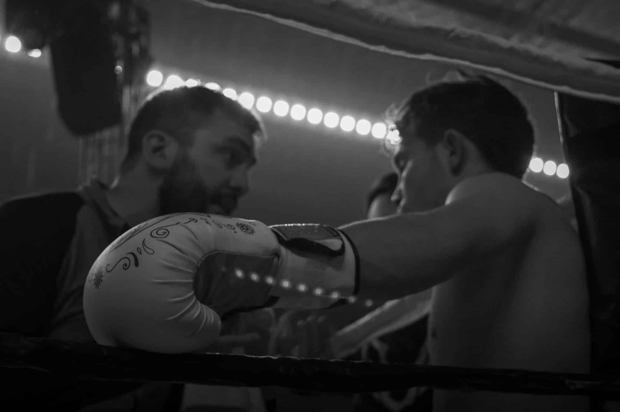 A boxer sitting on a chair, looking up at his coach who is speaking to him.