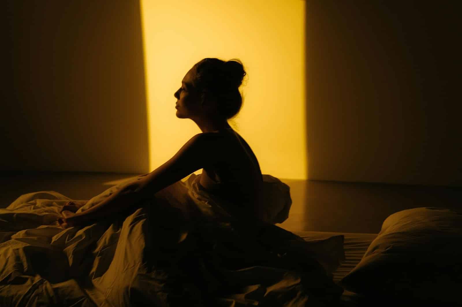 Woman on bed in shadow — "Mindfulness moment in solitude, free from screen distraction"