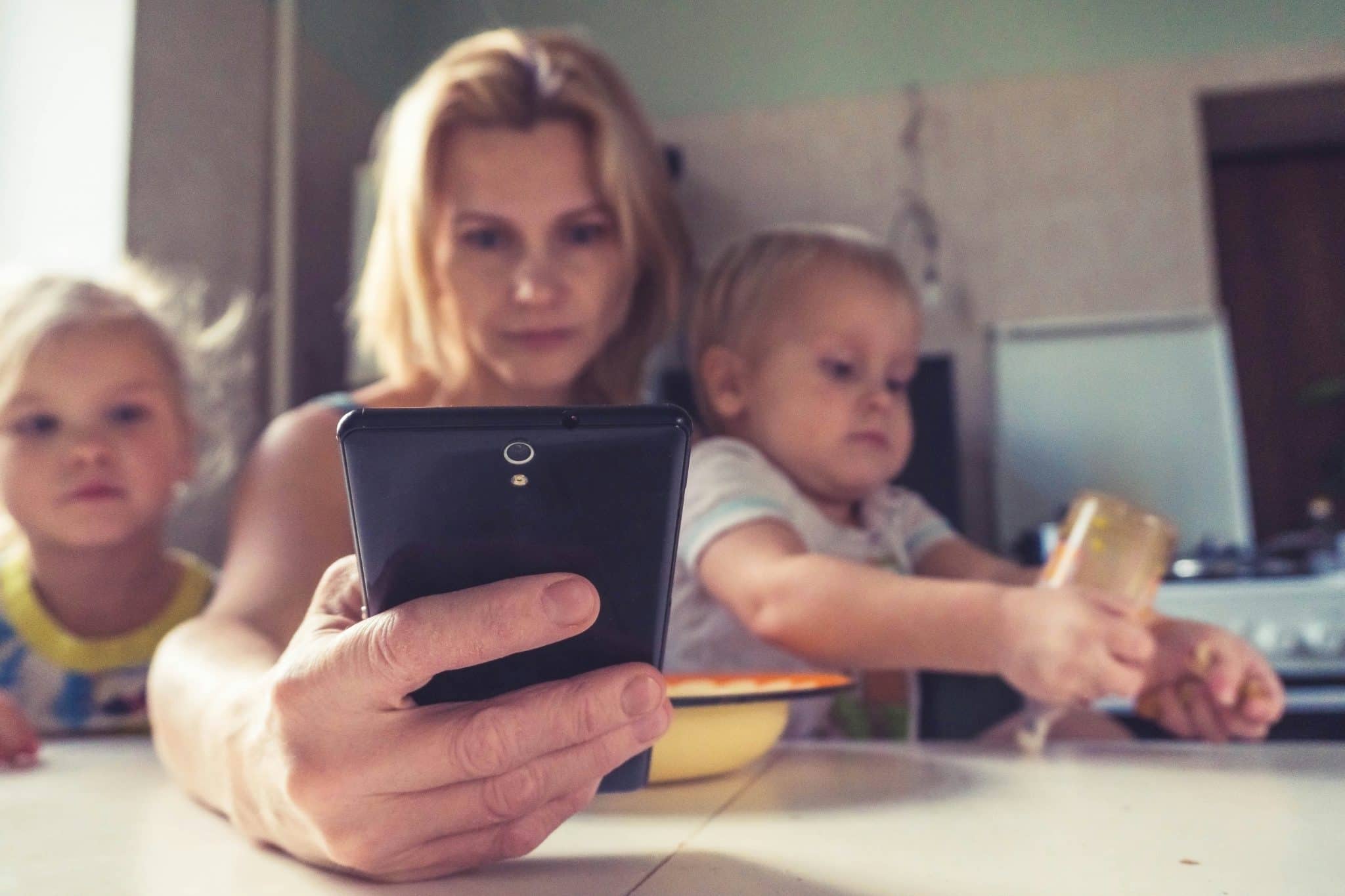 A woman looking overwhelmed and using a phone while dealing with her child, illustrating compulsive phone habits.