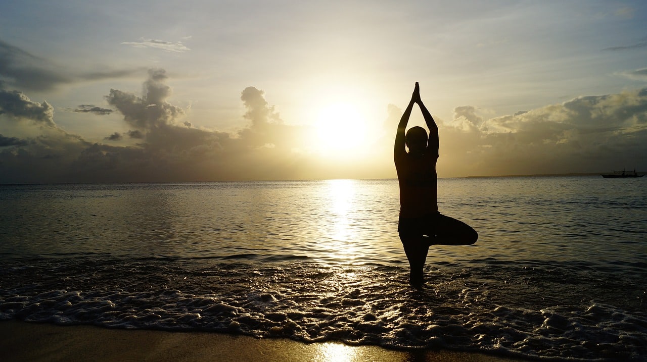 Silhouette of person doing yoga on the beach at sunset, representing fresh start habits and mindful movement.