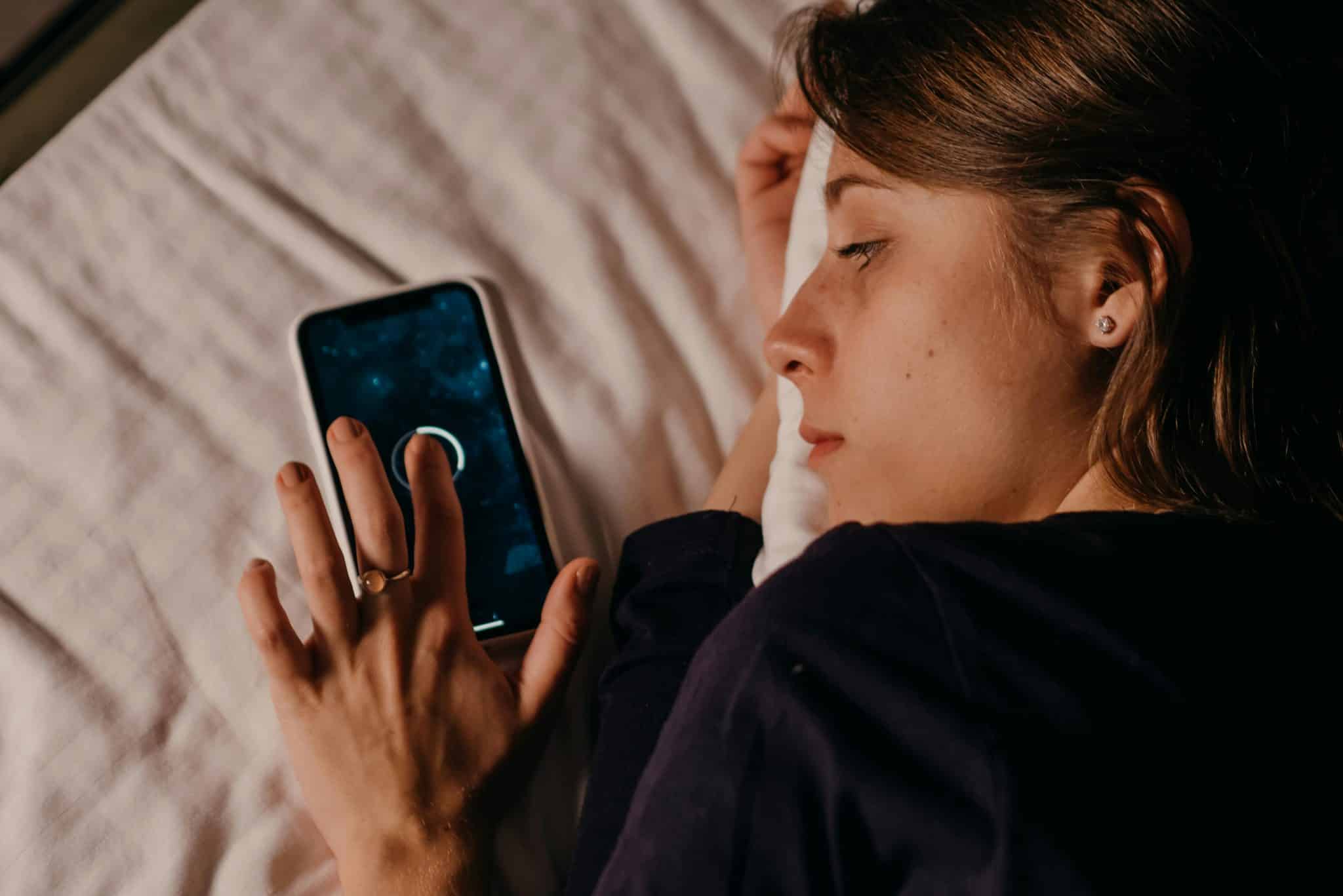 Woman using her phone in bed, illustrating how screen-time boundaries affect rest and late-night digital habits.