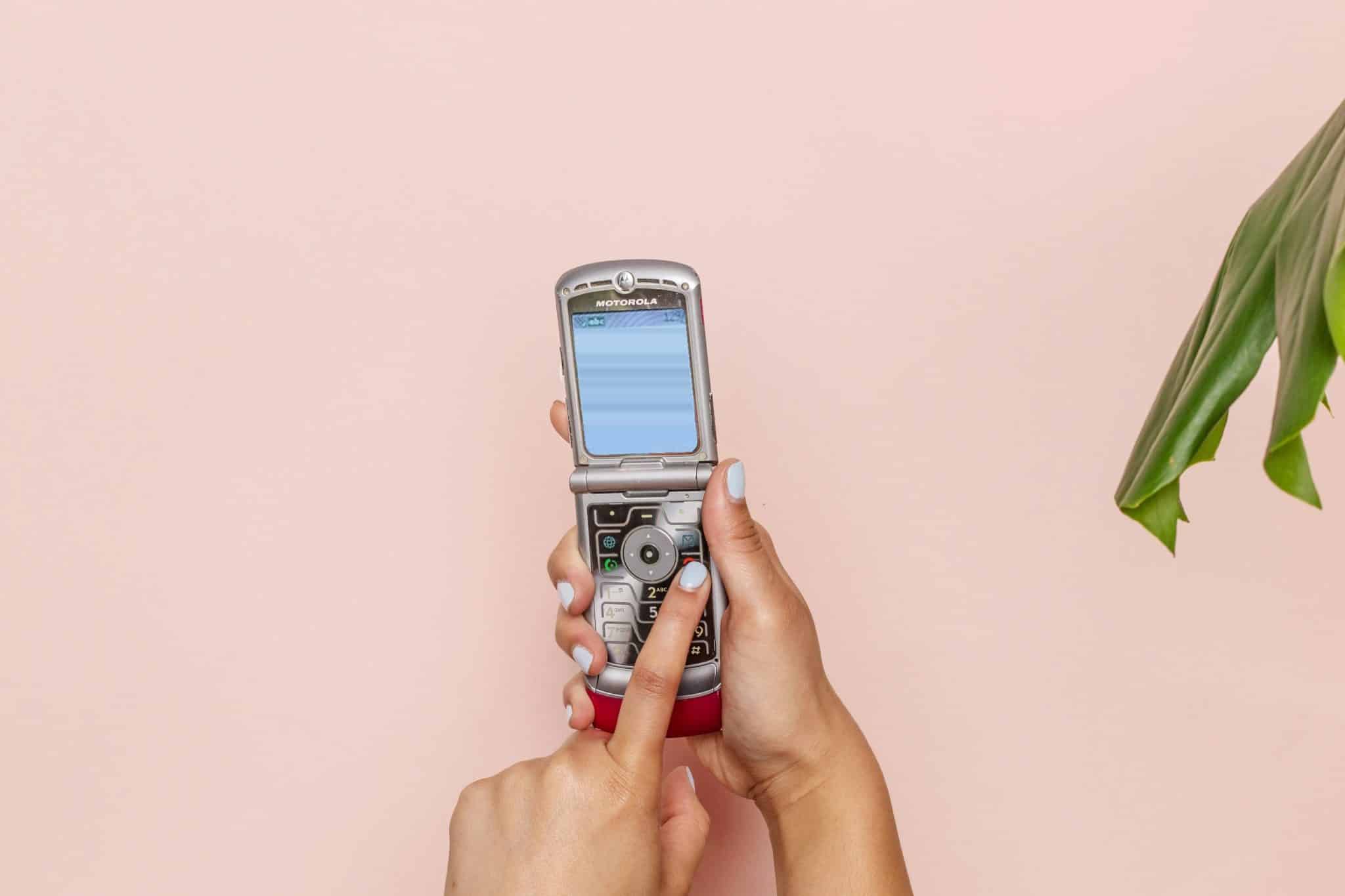 Hands holding an open silver Motorola flip phone against a pink wall